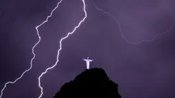 Petir menyambar di dekat patung Kristus Penebus di gunung Corcovado di Rio de Janeiro, Brasil, Selasa (21/2/2023). Pada 2007, Patung Yesus Kristus ini masuk dalam tujuh keajaiban dunia.  (Photo by MAURO PIMENTEL / AFP)