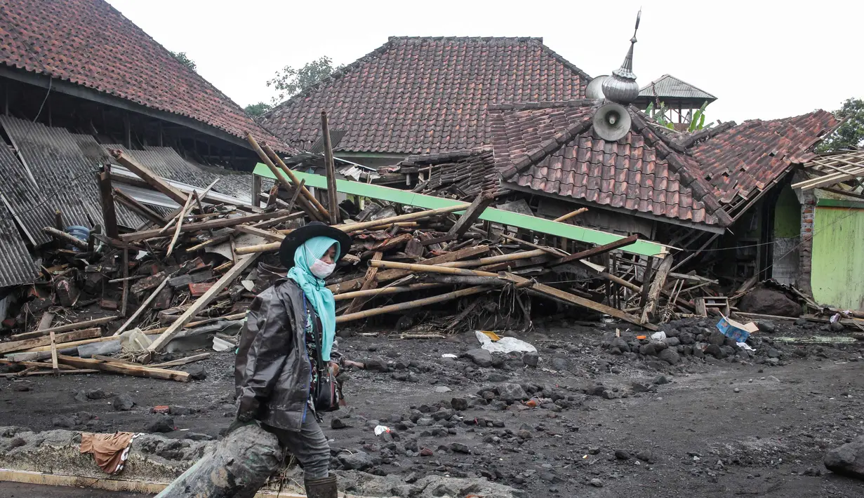 Seorang perempuan melintas di depan sebuah rumah yang hancur akibat aliran piroklastik Gunung Semeru di Desa Supiturang, Lumajang, Jawa Timur, pada Jumat 21 November 2025. Hari ketiga pasca-erupsi Gunung Semeru, atau Jumat (21/11/2025), Pemerintah Desa Supiturang, Kecamatan Pronojiwo, Kabupaten Lumajang, Jawa Timur, mencatat sedikitnya lebih dari 200 rumah dan fasilitas umum rusak parah. (Agus Harianto/AFP)