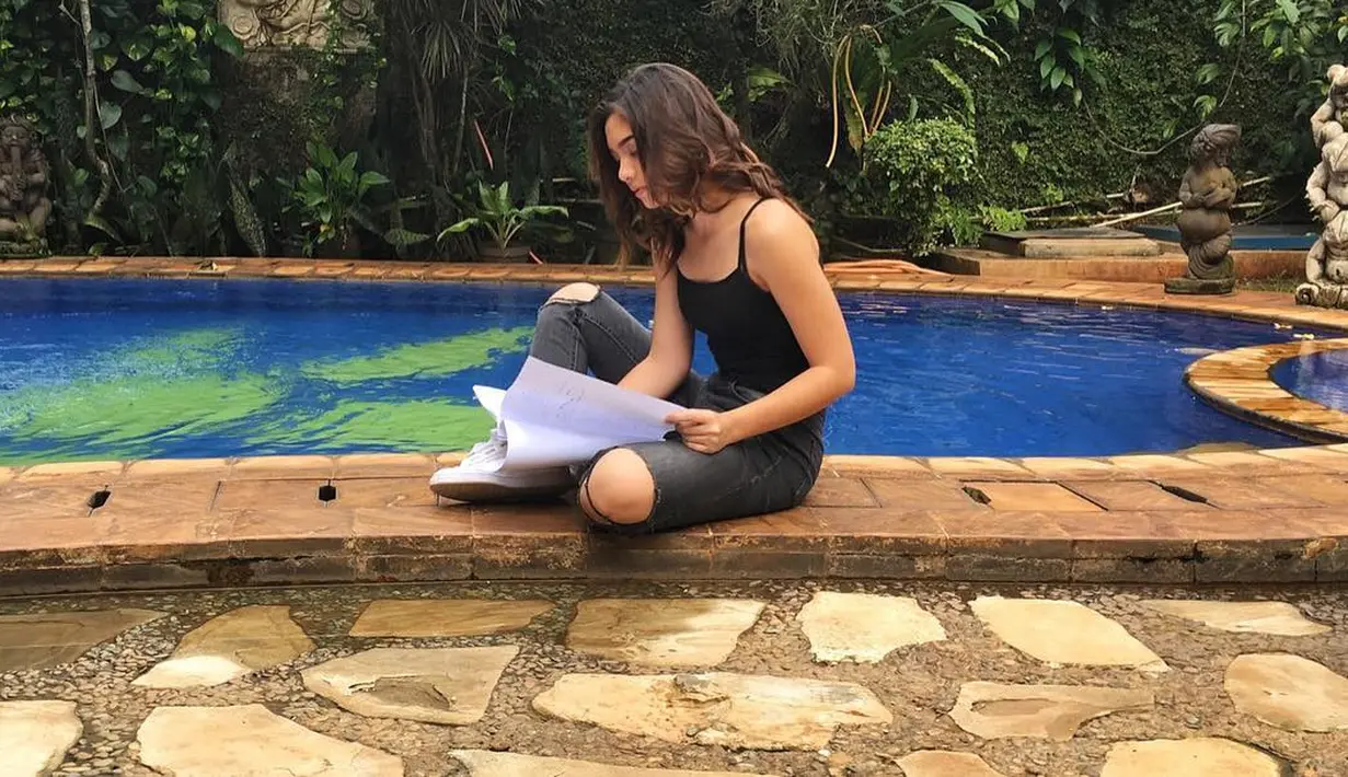 Nah, kalau yang satu ini sepertinya Agela Gilsha sedang proses membaca naskah skenarionya. Di pinggir kolam renang, Angela mengenakan outfit yang santai banget. Ia memadukan ripped jeans dengan tanktop hitamnya. (Instagram/angelagilsha)