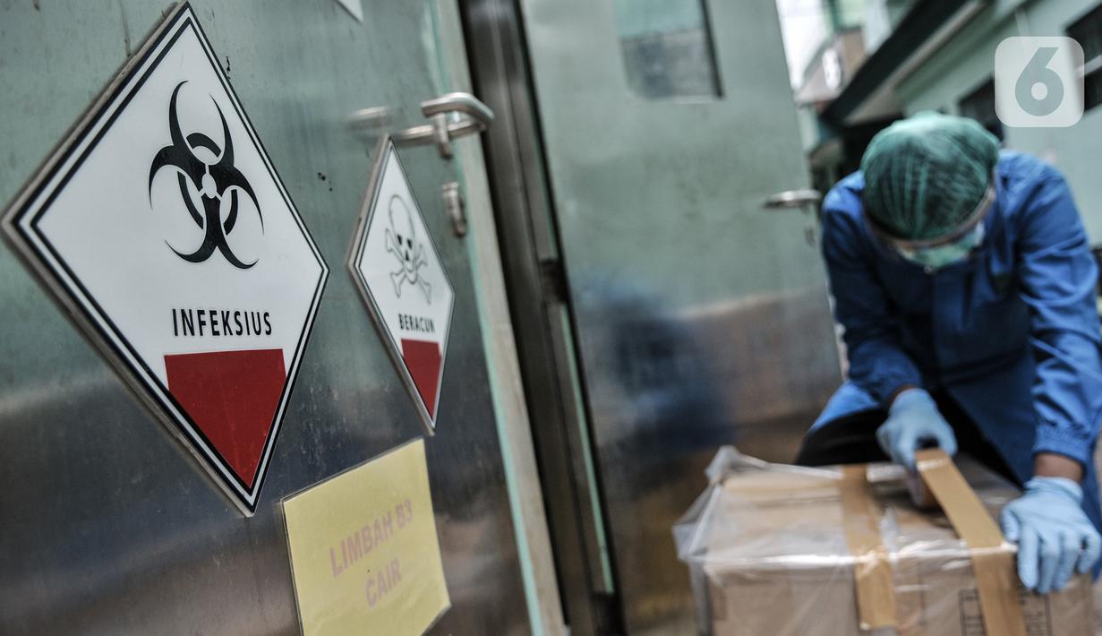 Petugas berpakaian APD mengemas limbah Covid-19 ke dalam kardus berlapis plastik di Tempat Penyimpanan Sementara Limbah B3 di Labkesda DKI Jakarta, Selasa (4/8/2020). Setiap kantong berisi limbah Covid-19 dibawa ke ruang sterilisasi sebelum diangkut ke tempat pembuangan. (merdeka.com/Iqbal Nugroho)