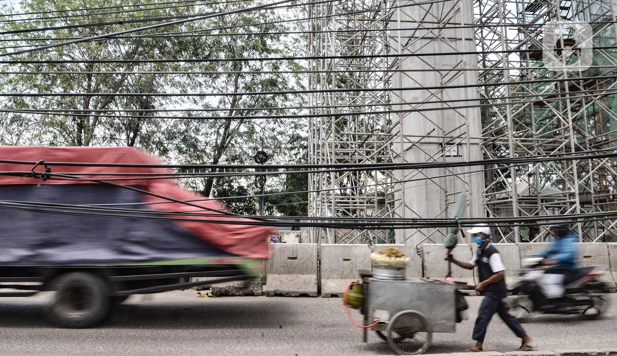 Pedagang melintas dekat instalasi kabel yang semrawut di Jalan Raya Bekasi, Cakung, Jakarta, Rabu (30/9/2020). Minimnya perawatan pascapembebasan lahan permukiman untuk proyek Tol Dalam Kota membuat jaringan kabel listrik di sepanjang jalan tersebut semrawut. (merdeka.com/Iqbal S. Nugroho)