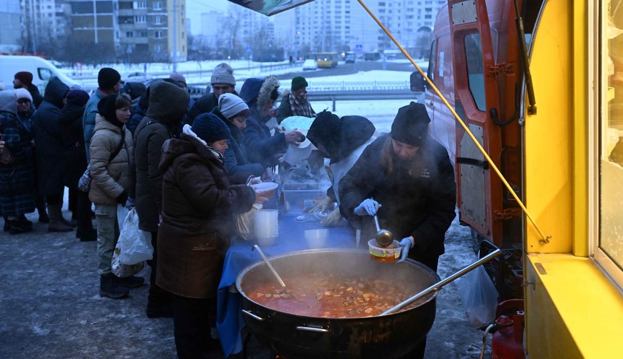Para sukarelawan dari organisasi amal makanan yang berbasis di Amerika Serikat (AS), World Central Kitchen, membagikan makanan hangat kepada warga setempat di sebuah kawasan perumahan di Kyiv yang mengalami pemadaman listrik dan air akibat serangan Rusia yang menghantam sektor energi, Kamis 22 Januari 2026. Serangan Rusia yang menghantam sektor energi melumpuhkan pasokan pemanas, listrik, dan air di ribuan bangunan permukiman di ibu kota Ukraina, Kyiv, ketika suhu udara turun hingga minus 14 derajat Celsius. (Sergei GAPON/AFP)