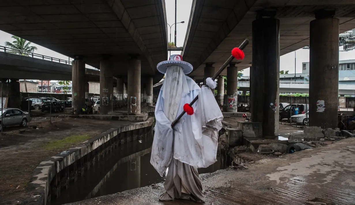 Seorang Eyo masqueraders mengenakan kostum dan penutup wajah berpose di bawah jembatan di jalan Lagos, Nigeria (20/5). (AFP Photo/Stefan Heunis)