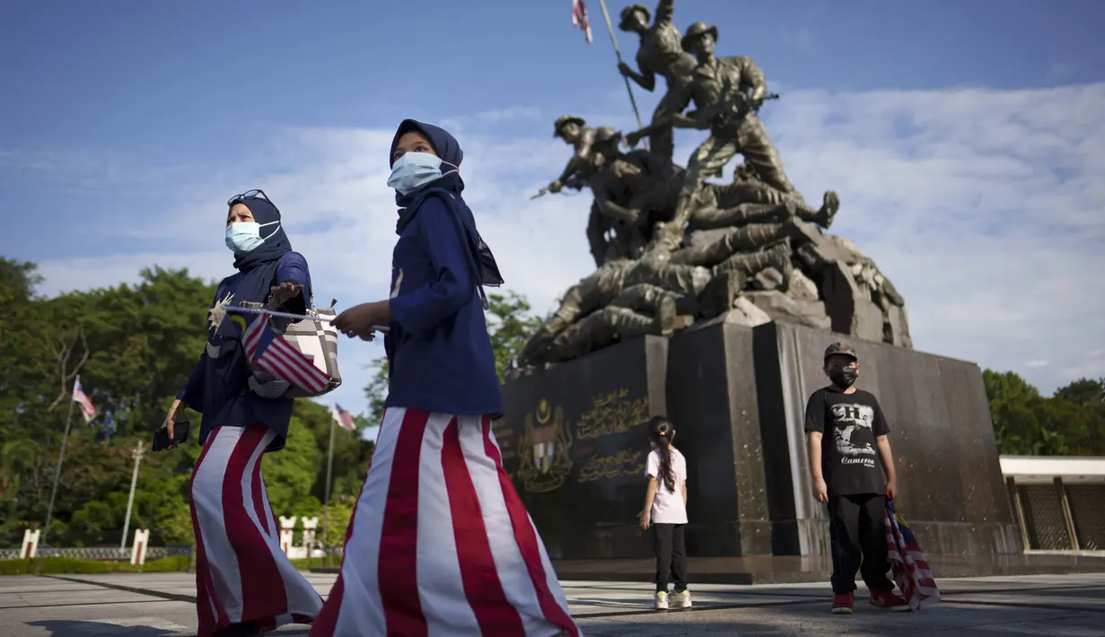 Dua muslimah mengenakan kostum bendera nasional Malaysia berjalan di depan Monumen Nasional saat perayaan Hari Nasional ke-64 untuk memperingati kemerdekaan dari penjajahan Inggris di Kuala Lumpur, Malaysia, Selasa (31/8/2021). (AP Photo/Vincent Thian)
