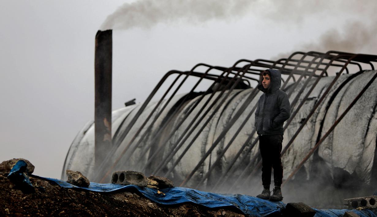 Amer al-Shayban (12) dari Suriah berdiri dekat cerobong asap saat dia bekerja di kilang minyak darurat dekat Kota al-Bab yang dikuasai Turki, Suriah, 20 November 2021. Menurut UNICEF, setelah satu dekade perang diperkirakan 2,5 juta anak-anak Suriah putus sekolah. (Bakr ALKASEM/AFP)