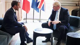 Presiden Prancis Emmanuel Macron berbincang dengan PM Inggris, Boris Johnson dalam kunjungan kenegaraan di Istana Elysee, Paris, Kamis (22/8/2019). Dalam pertemuan, Johnson tertangkap kamera bercanda ke arah kamera dan meletakkan kakinya di meja kopi. (Christophe Petit Tesson, Pool via AP)