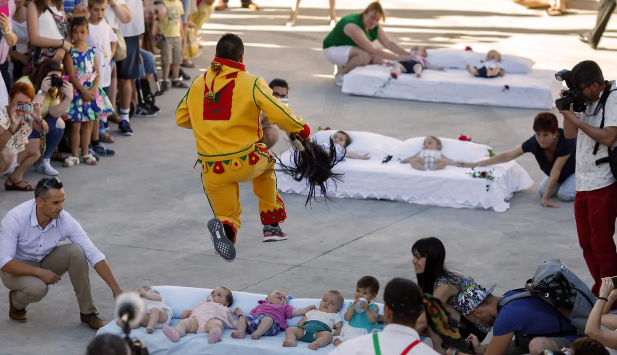 Pria berkostum setan melompati bayi-bayi yang terlentang di atas matras di sebuah jalan selama festival El Colacho di desa Castrillo de Murcia, Spanyol, Minggu (18/6). Tindakan ini bermakna untuk membersihkan bayi dari roh-roh jahat. (CESAR MANSO/AFP)
