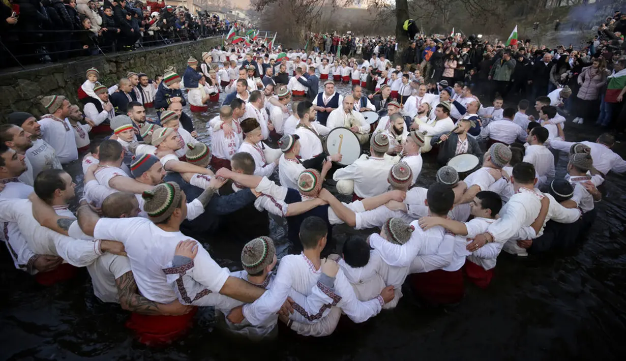 Para pria bernyanyi dan menari saat merayakan Epiphany di Sungai Tundzha, Kalofer, Bulgaria, 6 Januari 2022. Epiphany adalah sebuah hari raya keagamaan dalam sejumlah denominasi gereja Kristen pada tanggal 6 Januari. (AP Photo/Valentina Petrova)