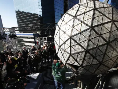 Awak media melihat pekerja menyelesaikan pemasangan bola kristal di atas sebuah gedung di Times Square, New York, Kamis (27/12). Menyaksikan bola kristal raksasa adalah tradisi yang tidak terlewatkan setiap perayaan tahun baru sejak 1907. (AP/Seth Wenig)