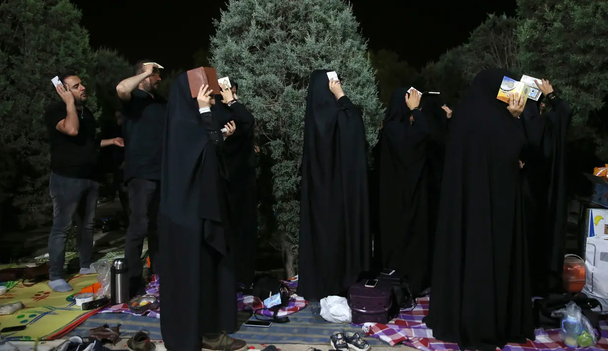 Umat Syiah Iran mengenakan pakaian berwarna hitam menempatkan salinan Al Quran diatas kepala mereka saat berdoa pada malam Ramadan di Teheran, Iran (16/6). Mereka membaca Al Quran dan berdoa untuk meminta pengampuan. (AP Photo/Vahid Salemi)