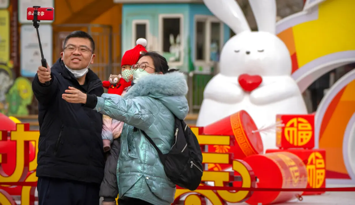 Sebuah keluarga berswafoto dengan patung kelinci saat pekan liburan Tahun Baru Imlek di taman umum di Beijing, China, Kamis (26/1/2023). (AP Photo/Mark Schiefelbein)
