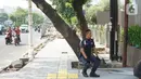 Petugas kemanan duduk dekat pohon yang berada di jalur pedestrian Jalan Kramat Raya, Jakarta, Jumat (8/11/2019). Sepanjang pengerjaan jalur pedestrian, pohon yang berada di jalur tersebut rencananya juga akan direvitalisasi dan diremajakan. (Liputan6.com/Immanuel Antonius)
