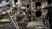 Seorang prajurit Ukraina berbicara di telepon di depan sebuah bangunan tempat tinggal yang rusak puing setelah peluru militer Rusia menghantam bangunan di Koshytsa Street, Kiev, Ukraina (25/2/2022). (AFP/Daniel Leal)