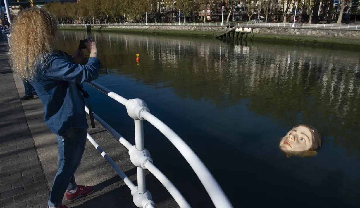Seorang wanita mengambil gambar patung Bihar karya seniman hiperrealis asal Meksiko Ruben Orozco yang terendam di Sungai Nervion, Kota Bilbao, Basque, Spanyol, 14 Oktober 2021. Patung perempuan duduk sendirian di bangku taman juga pernah memicu perdebatan di Bilbao. (ANDER GILLENEA/AFP)