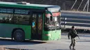 Sebuah bus yang digunakan untuk mengevakuasi warga sipil melewati seorang anggota pasukan Presiden Suriah Bashar al-Assad, meninggalkan wilayah yang dikuasai pemberontak di Aleppo, Suriah, Kamis (15/12). (REUTERS/Omar Sanadiki)
