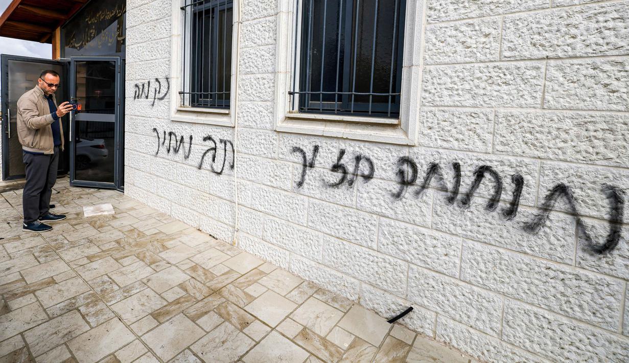 Para pemukim ilegal Israel juga mencoret dinding Masjid Abu Bakr as-Siddiq yang berada di antara Sarra dan Tal, dekat Nablus, wilayah utara Tepi Barat, dengan slogan-slogan rasis. Tampak dalam foto, seorang pria merekam coretan grafiti Ibrani pada dinding luar Masjid Abu Bakr al-Siddiq di desa Tell, sebelah barat Nablus, Tepi Barat yang diduduki, pada 23 Februari 2026. (JAAFAR ASHTIYEH/AFP)