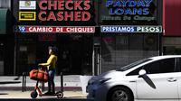 Seseorang mengendarai skuter melewati toko pencairan cek dan pinjaman gaji di pusat kota Los Angeles, California, Jumat (11/3/2022). Laju inflasi AS pada Februari 2022 melonjak ke level tertinggi dalam 40 tahun. Ini didorong naiknya harga bensin, makanan dan perumahan. (Patrick T. FALLON/AFP)