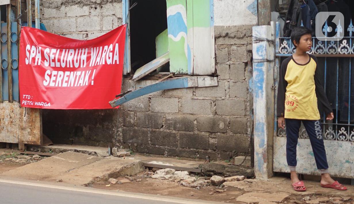 Seorang anak berdiri dekat poster protes warga terhadap pembangunan flyover di kawasan Tanjung Barat, Jakarta, Rabu (15/7/2020). Dalam poster protes tersebut, warga menuntut agar pembayaran pelunasan pembebasan lahan segera diselesaikan secara serentak. (Liputan6.com/Immanuel Antonius)