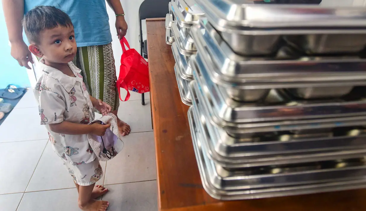 Seorang anak menemani ibunya mengambil makan bergizi gratis (MBG) untuk dikonsumsi di rumah di Posyandu kawasan Limo, Depok, Jawa Barat, Selasa (14/7/2025).
