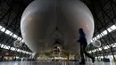 Petugas berjalan di depan The Airlander 10 saat peluncuran media di Cardington Airfield, Bedfordshire, Senin (21/3). Pesawat ini memiliki panjang  90 meter dan mempunyai lambung besar yang bisa dimasuki sebuah pesawat komersial. (ADRIAN DENNIS/AFP)