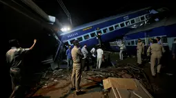 Aparat kepolisian India berdiri dekat gerbong kereta Kalinga-Utkal Express yang tergelincir hingga keluar jalur di Negara Bagian Uttar Pradesh, Minggu (20/8). Beberapa gerbong yang tergelincir menghantam rumah-rumah di dekatnya. (AP/Altaf Qadri)