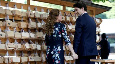  Perdana Menteri Kanada Justin Trudeau bersama istrinya Sophie Gregoire Trudeau saling pegangan tangan saat mereka mengantungkan 'Ema' atau sebuah harapan yang mereka tulis di sebuah kayu di Kuil Meiji di Tokyo, Jepang (24/5).  (REUTERS/Issei Kato)