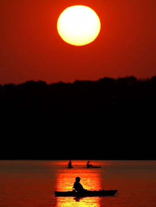 Orang-orang menyaksikan matahari terbenam sambil berperahu di Shawnee Mission Lake, Shawnee, Kansas, Amerika Serikat, Jumat (9/10/2020). Matahari terbenam terus lebih cerah dari biasanya karena asap dari kebakaran hutan barat terus melayang di seluruh negeri. (AP Photo/Charlie Riedel)