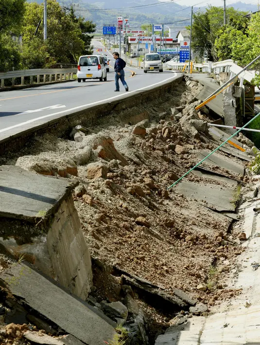 Seorang pria berjalan di dekat jalan yang rusak pasca gempa bumi di kota Mashiki, Prefektur Kumamoto, Jepang selatan, Jumat (15/4). Gempa 6,4 SR yang terjadi Kamis (14/4) itu juga mengakibatkan lebih dari 20 bangunan rumah hancur. (REUTERS/Kyodo)