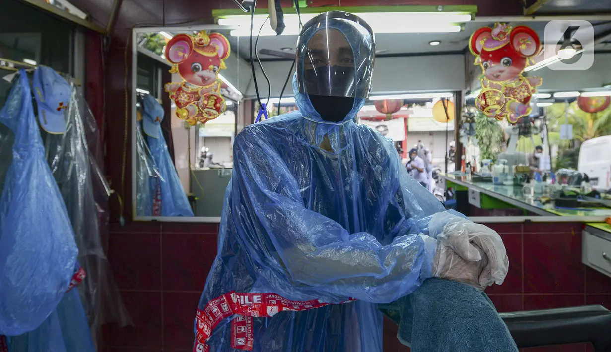 Tukang cukur mengenakan alat pelindung diri (APD) dari plastik bersiap mencukur rambut pelanggan di Pondok Kelapa, Jakarta, Selasa (5/5/2020). Tukang cukur mengenakan APD untuk mengurangi risiko penularan virus corona COVID-19. (merdeka.com/Imam Buhori)