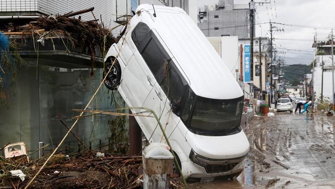 Sebuah mobil bersandar pada bangunan menyusul hujan lebat di Hitoyoshi, prefektur Kumamoto, Jepang, Senin (6/7/2020). Banjir di wilayah Kumamoto yang memicu tanah longsor ini telah menghancurkan ratusan rumah dan kendaraan serta membuat jembatan antar kota terputus. (Yuki Sato/Kyodo News via AP)