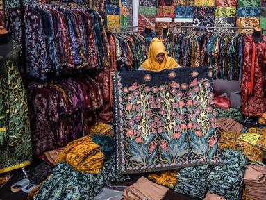 Seorang wanita menunjukkan selembar kain batik di ruang pamer di Sidoarjo, Jawa Timur, Sabtu (1/10/2022). Indonesia akan memperingati Hari Batik Nasional pada 2 Oktober. (JUNI KRISWANTO/AFP)