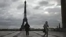Orang-orang yang memakai masker berjalan di alun-alun Trocadero, dekat Menara Eiffel, di Paris, Kamis (19/11/2020). Prancis telah melampaui 2 juta kasus virus corona COVID-19 yang dikonfirmasi, total tertinggi keempat di dunia. (AP Photo/Michel Euler)