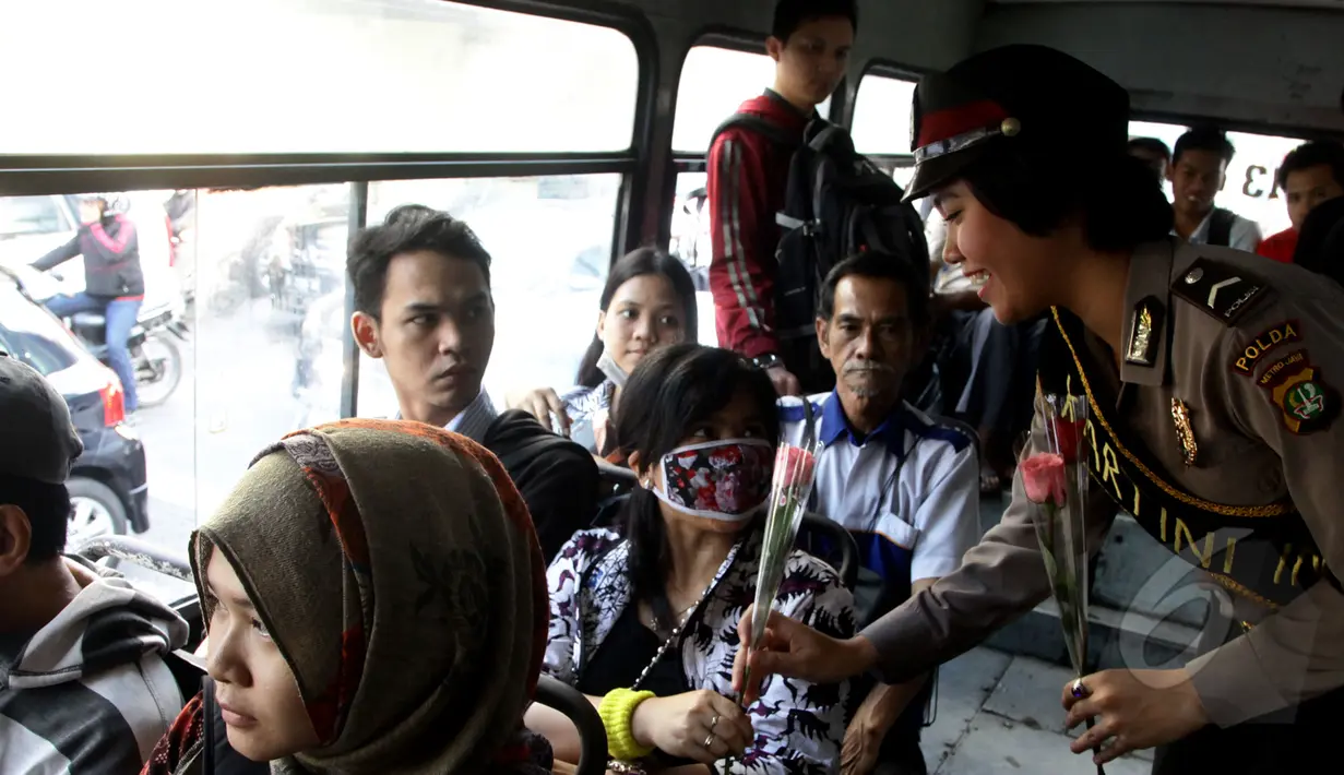 Seorang anggota Polwan membagikan bunga pada penumpang bis kota di kawasan Slipi, Jakarta, Selasa (21/4/2015). Pembagian bunga ini dalam rangka memperingati hari Kartini.(Liputan6.com/Johan Tallo)