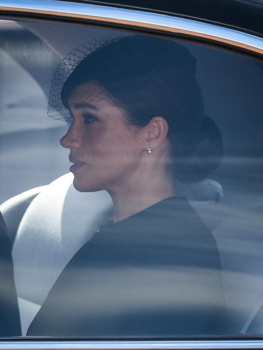 Meghan Markle berada di dalam mobil saat menghadiri prosesi persemayaman Ratu Elizabeth II di Westminster Hall di London (14/9/2022). Anting-anting ini dikenakan wanita 41 tahun tersebut saat ia melakukan tugas kerajaan pertama bersama Ratu Elizabeth II, tanpa Pangeran Harry. (Photo by Daniel LEAL/various sources/AFP)