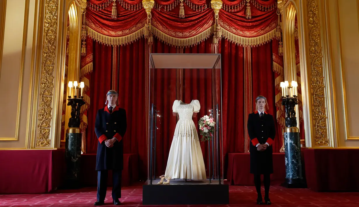 Petugas kerajaan berdiri di samping gaun pengantin Putri Beatrice yang dipajang di Kastil Windsor, Windsor, Rabu (23/9/2020). Beatrice menikah dalam balutan gaun pengantin dari era tahun 1960-an rancangan Norman Hartnell yang dipinjamkan sang nenek, Ratu Elizabeth II. (AP Photo/Kirsty Wigglesworth)
