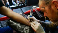 Seorang seniman tato membuat gambar lebah di pergelangan tangan seorang Mancunian di Manchester (28/5). Seniman ini membuat tato lebah untuk menggalang dana yang diberikan kepada korban serangan bom konser Ariana Grande. (AP Photo/Mstyslav Chernov)