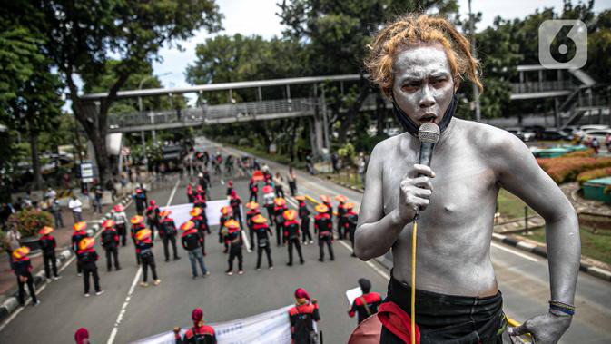 Seorang buruh dengan tubuh di cat silver berorasi saat unjuk rasa di kawasan Patung Kuda, Jakarta, Rabu (16/12/2020). Aksi yang dihadiri ratusan buruh ini mematuhi imbauan pemerintah terkait protokol kesehatan. (Liputan6.com/Faizal Fanani)