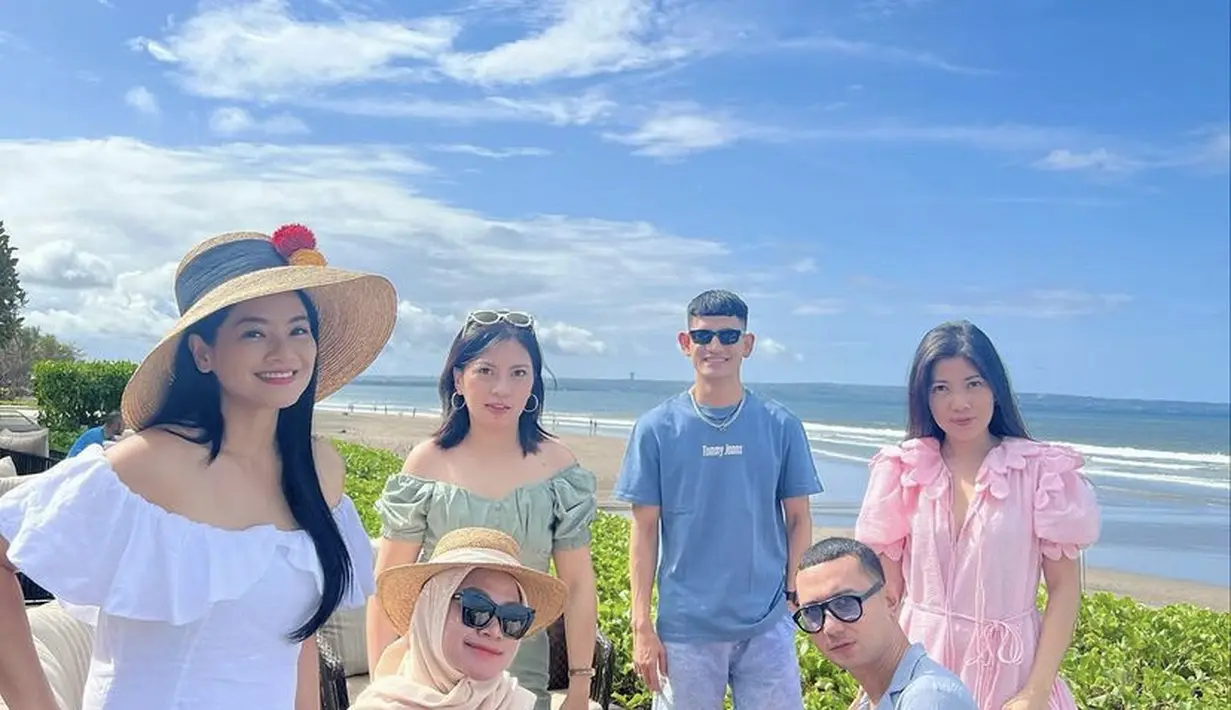 Berada di pinggir pantai, Titi Kamal bersama sahabat tampil mengenakan mini dress off shoulder putih. Rambut panjang hitamnya ditutupi dengan topi pantai cokelat.  (@titi_kamall)