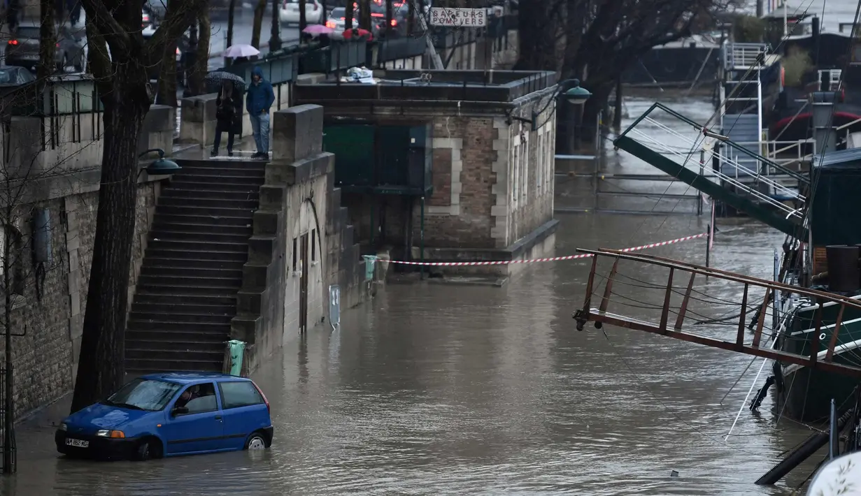 Sebuah mobil melintasi banjir di tepi sungai Seine, Paris (22/1). Sungai Seine telah berubah menjadi torrent berlumpur yang kuat yang telah menenggelamkan taman dan jalan. (AFP Photo/Stephane De Sakutin)