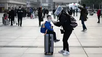 Seorang wanita yang mengenakan masker, sarung tangan, dan pelindung wajah menyesuaikan masker anaknya di Stasiun Hankou, Wuhan, Hubei, China, Rabu (8/4/2020). Setelah pandemi virus corona COVID-19 mereda, banyak warga di Wuhan beraktivitas memakai alat pelindung diri. (NOEL CELIS/AFP)
