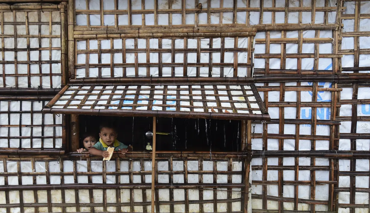 Anak-anak pengungsi Rohingya melihat keluar dari rumah saat hujan lebat di kamp pengungsi Kutupalong di Ukhia 12/9/2019). Kamp ini adalah salah satu dari dua kamp pengungsi yang dikelola pemerintah di Cox's Bazar, kamp yang satunya lagi adalah kamp pengungsi Nayapara. (AFP Photo/Munir Uz Zaman)