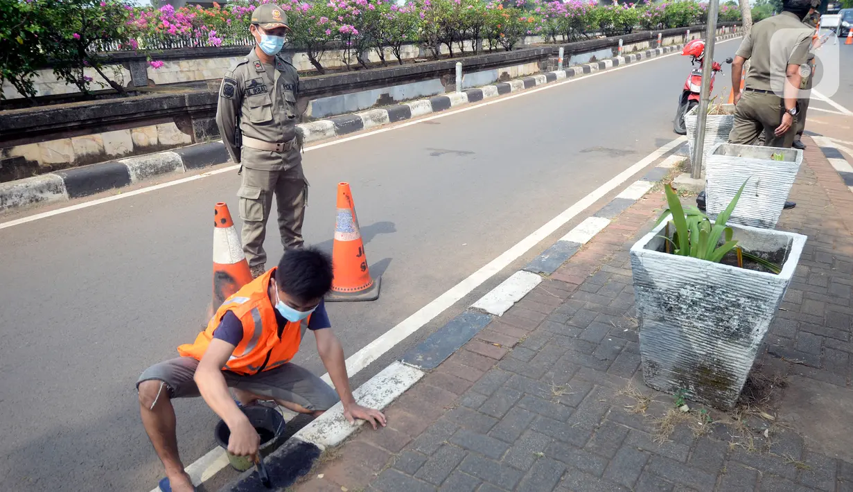 Petugas Satpol PP memberikan sanksi sosial mengcat pembatas jalan kepada warga pelanggar karena tidak menggunakan masker di Lebak Bulus, Jakarta, senin (14/09/2020). Pemerintah Provinsi DKI Jakarta memperketat kembali PSBB karena kasus Covid-19 terus mengalami peningkatan. (merdeka.com/Dwi Narwoko)