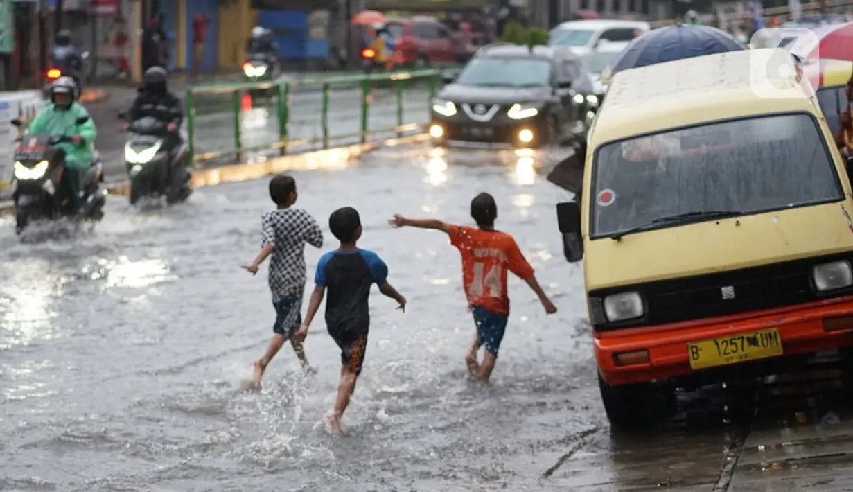 Anak-anak melintasi banjir yang menggenangi Jalan Arif Rahman Hakim di Depok, Jawa Barat, Senin (18/5/2020). Sistem drainase buruk menjadi penyebab utama kawasan tersebut selalu tergenang banjir setiap hujan deras. (Liputan6.com/Immanuel Antonius)