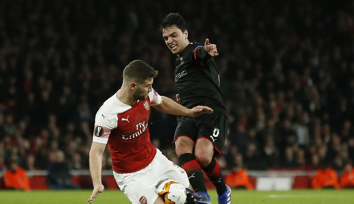 Aaron Ramsey mencoba menghentikan Gerzino Nyamsi pada leg kedua,babak 16 besar Liga Europa yang berlangsung di Stadion Emirates, London, Jumat (15/3). Arsenal menang 3-0 atas Rennes. (AFP/Ian Kington)