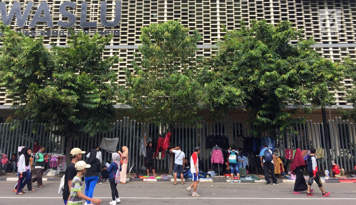 Pedagang kaki lima (PKL) menggantungkan pakaian-pakaian dagangannya di pagar kantor saat pelaksanaan car free day (CFD) di Jakarta, Minggu (11/2). (Liputan6.com/Immanuel Antonius)
