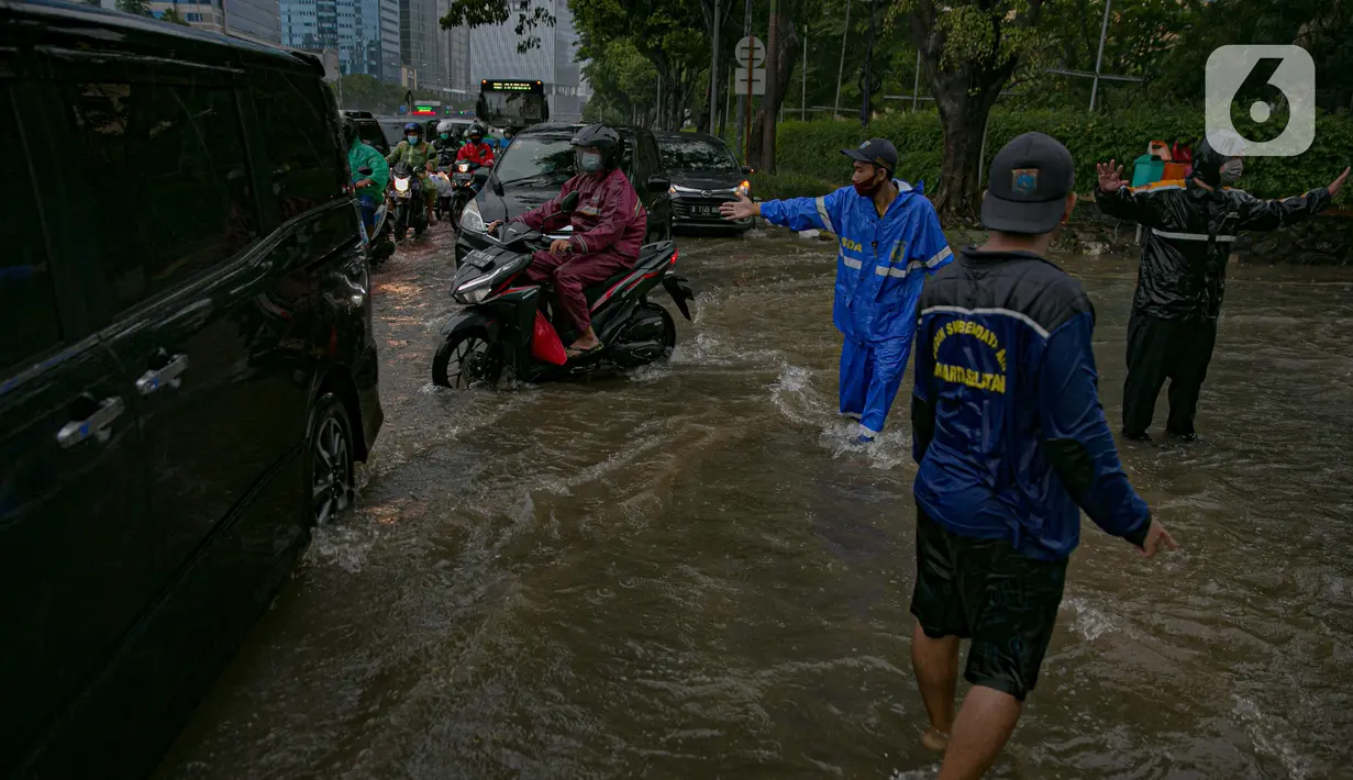 Petugas mengatur kelancaran lalu lintas saat air menggenangi ruas Jalan Gatot Subroto, Jakarta, Kamis (18/2/2021). Hujan deras yang mengguyur wilayah Jakarta menyebabkan terjadinya genangan di beberapa ruas jalan, meski begitu sejauh ini kendaraan masih dapat melintas. (Liputan6.com/Faizal Fanani)