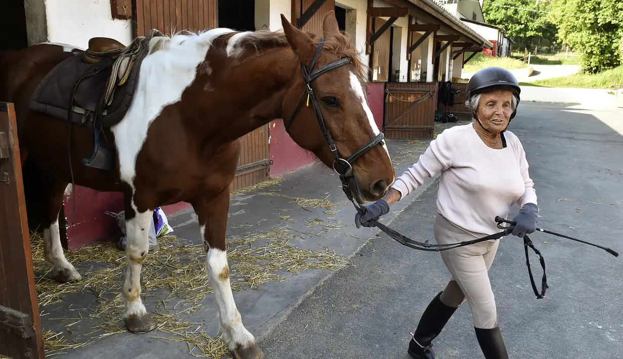 Nicole de Villeneuve (89) bersiap berlatih berkuda selama sesi pelatihan di Arcachon, Prancis (24/4). Seorang wanita cantik dengan mata hijau-biru mengatakan "Obatku adalah kuda, aku lupa segalanya,". (AFP Photo/Georges Gobet)