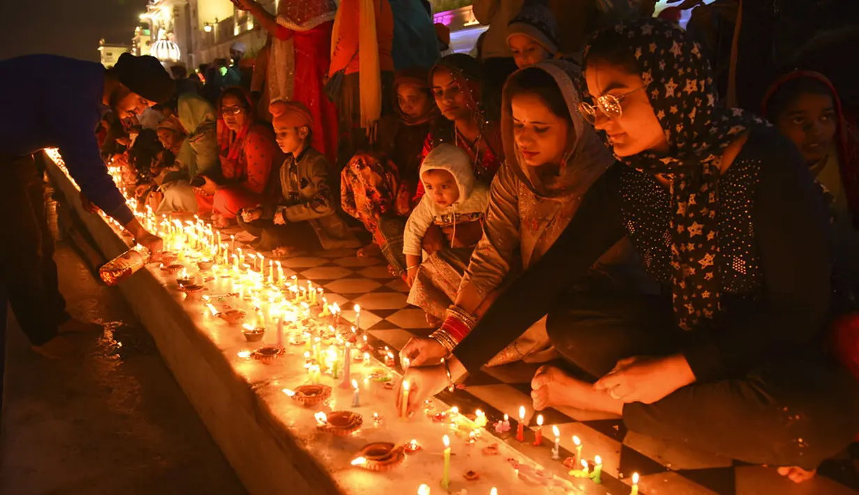 Umat Sikh menyalakan lampu tanah di Kuil Emas yang diterangi pada peringatan kelahiran Guru Nanak di Amritsar, India, 19 November 2021. Guru Nanak adalah Guru Sikh pertama dan pendiri Sikhisme. (AP Photo/Prabhjot Gill)