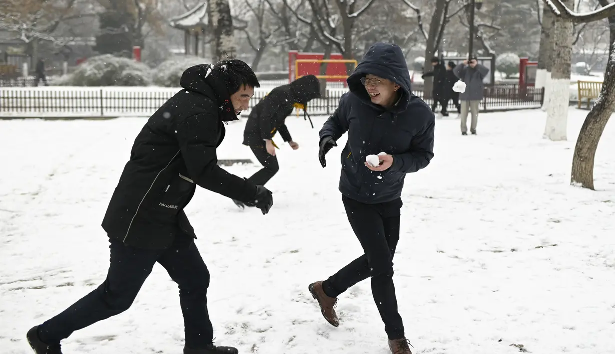Orang-orang bermain bola salju saat salju turun di sebuah taman di Beijing (16/12/2019). Beijing mengeluarkan peringatan biru untuk salju tebal pada hari Minggu, yang merupakan yang terendah dalam sistem peringatan empat tingkat ibu kota. (AFP Photo/Wang Zhao)
