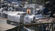 Truk-truk yang mengangkut bantuan yang masuk ke Jalur Gaza melalui pos perbatasan Karm Abu Salem, melintas di dekat tenda-tenda pengungsian di kamp pengungsi Nuseirat di bagian tengah Jalur Gaza, pada Selasa 14 Oktober 2025. (Eyad BABA/AFP)